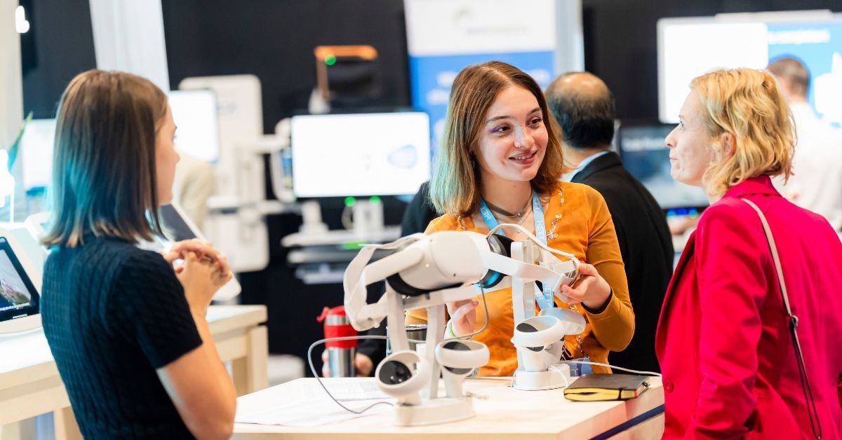 3 women networking at an exhibitor stand with vr headsets on the table