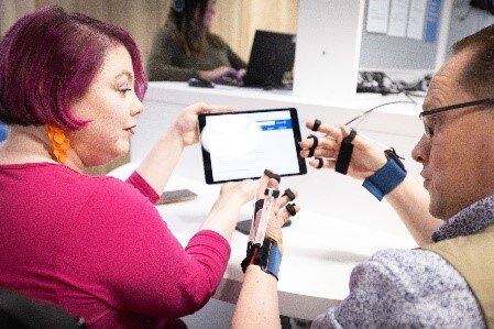 A man wearing gloves that make his hands stiff and hard to move, trying to use a tablet computer